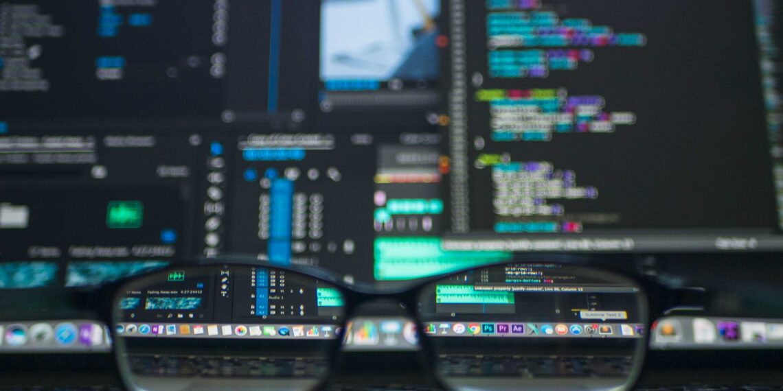 számítógép képernyőjén kódok és előtte az asztalon szemüveg