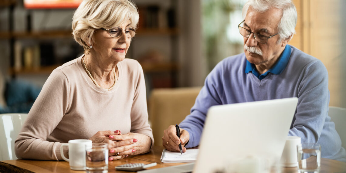 nyugdíjas pár laptopot és jegyzetet használ a nyugdíjbiztosításuk kalkulációjához